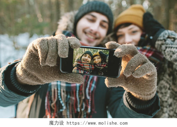 年轻的时髦夫妇以自拍照在冬季森林与智能手机